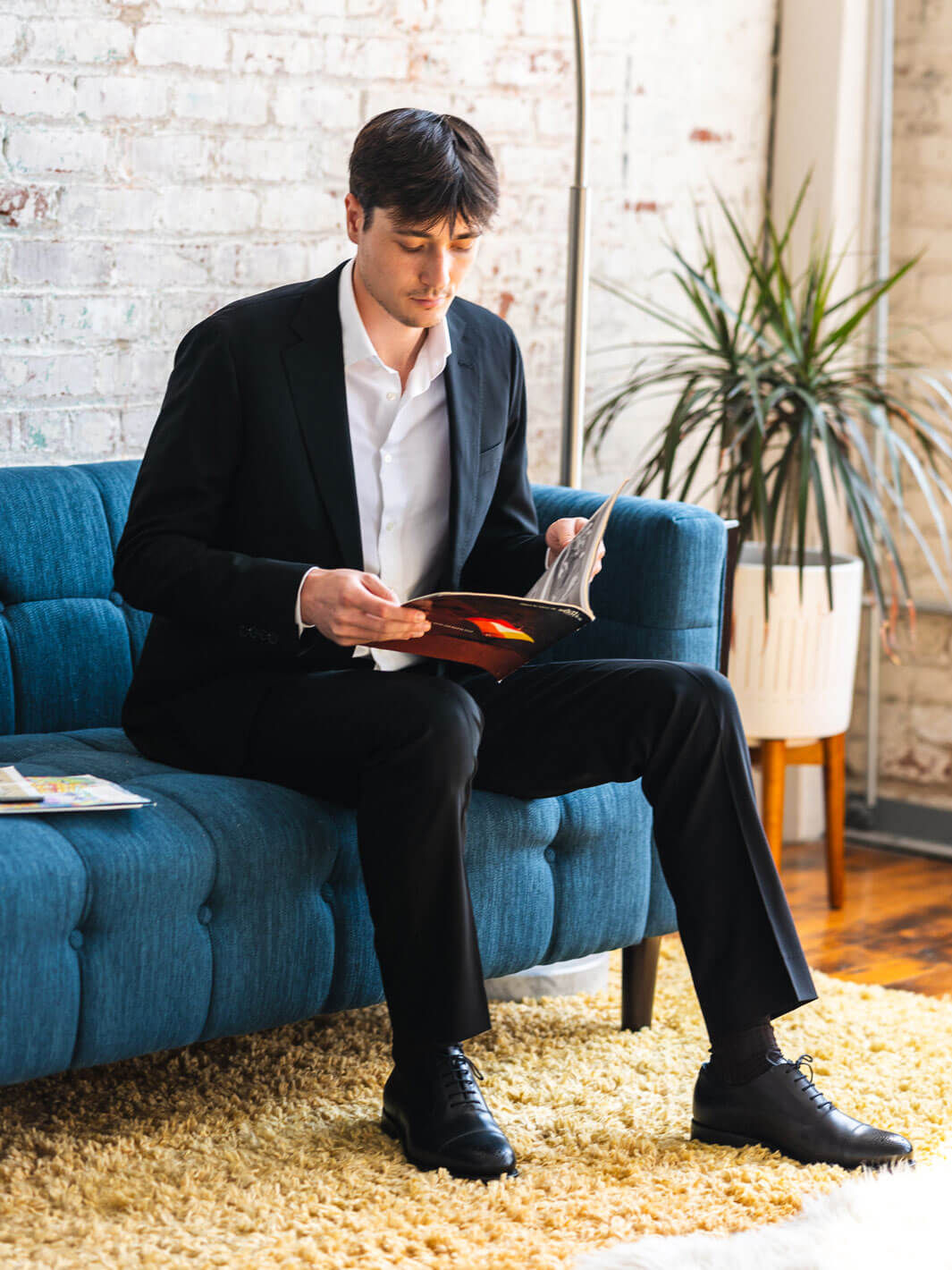 picture of man sitting on blue couch wearing a deep black suit by Anatoly & Sons