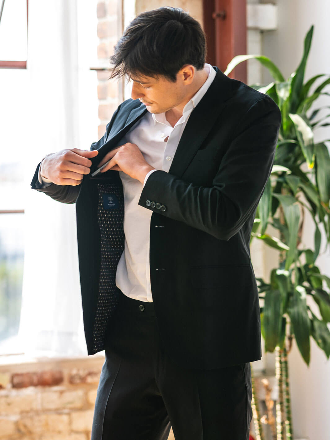 A man wearing Anatoly & Sons' deep black suit gracefully opens the jacket, sliding his phone into the sleek interior pocket