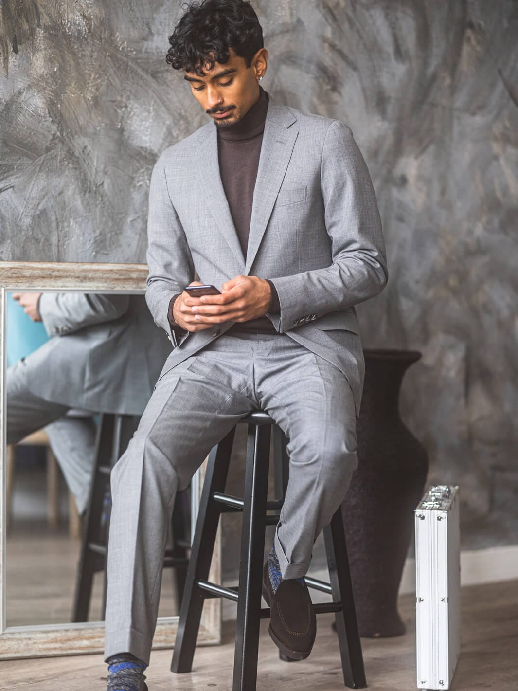 Man sitting on stool looking at phone while wearing Anatoly & Sons Light Grey Skyfall Suit